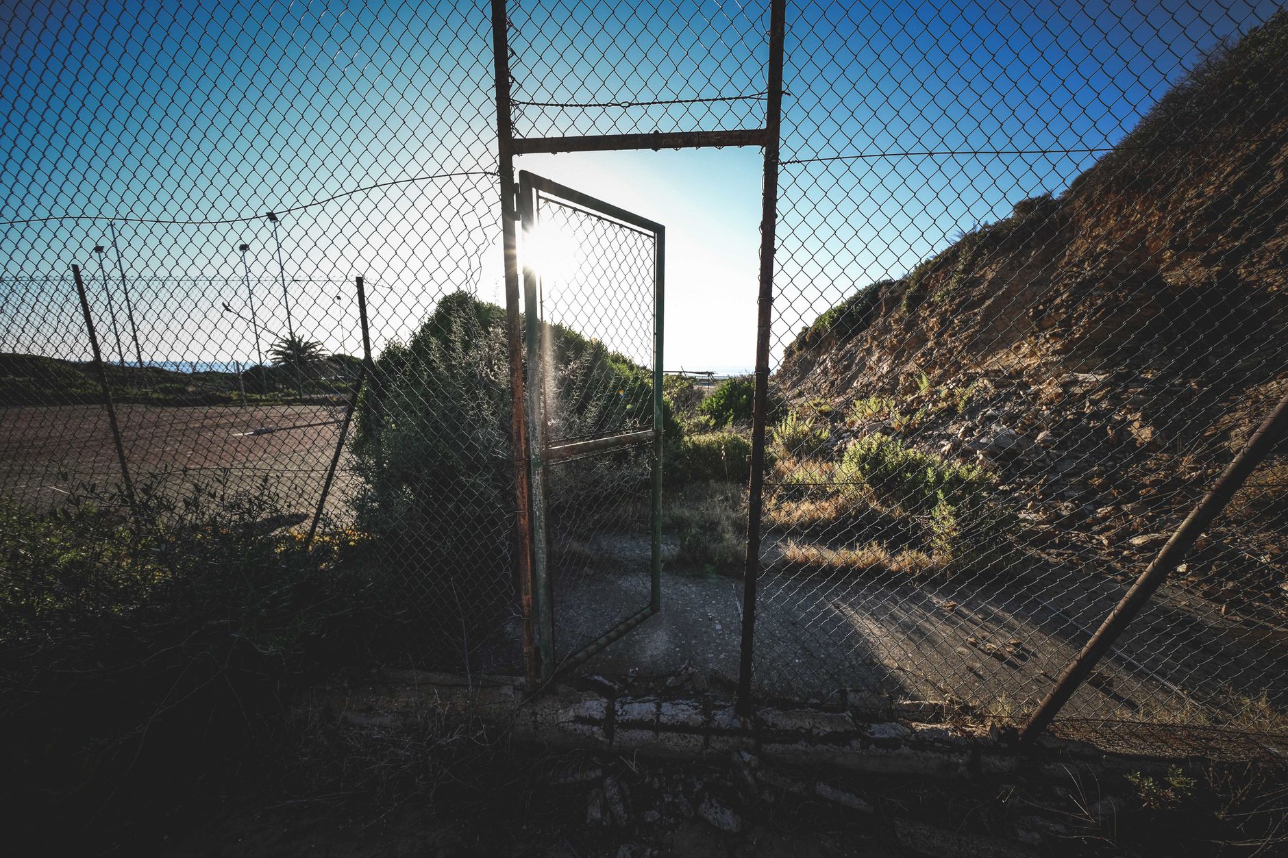 Old rusty chain link fence near rough mountain against cloudless blue sky on sunny day