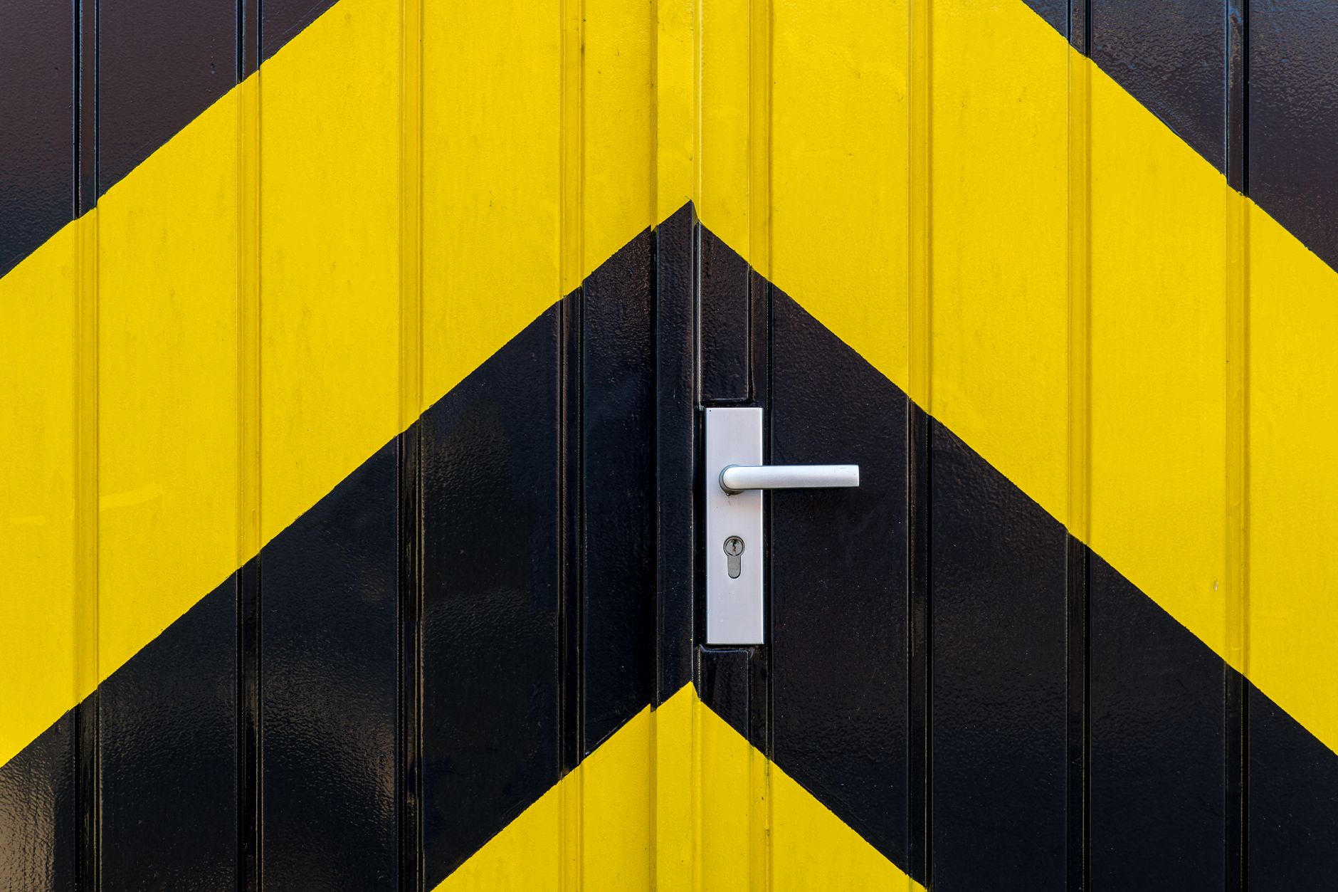 Close-up shot of a metal door with bold yellow and black chevron patterns and a modern silver handle