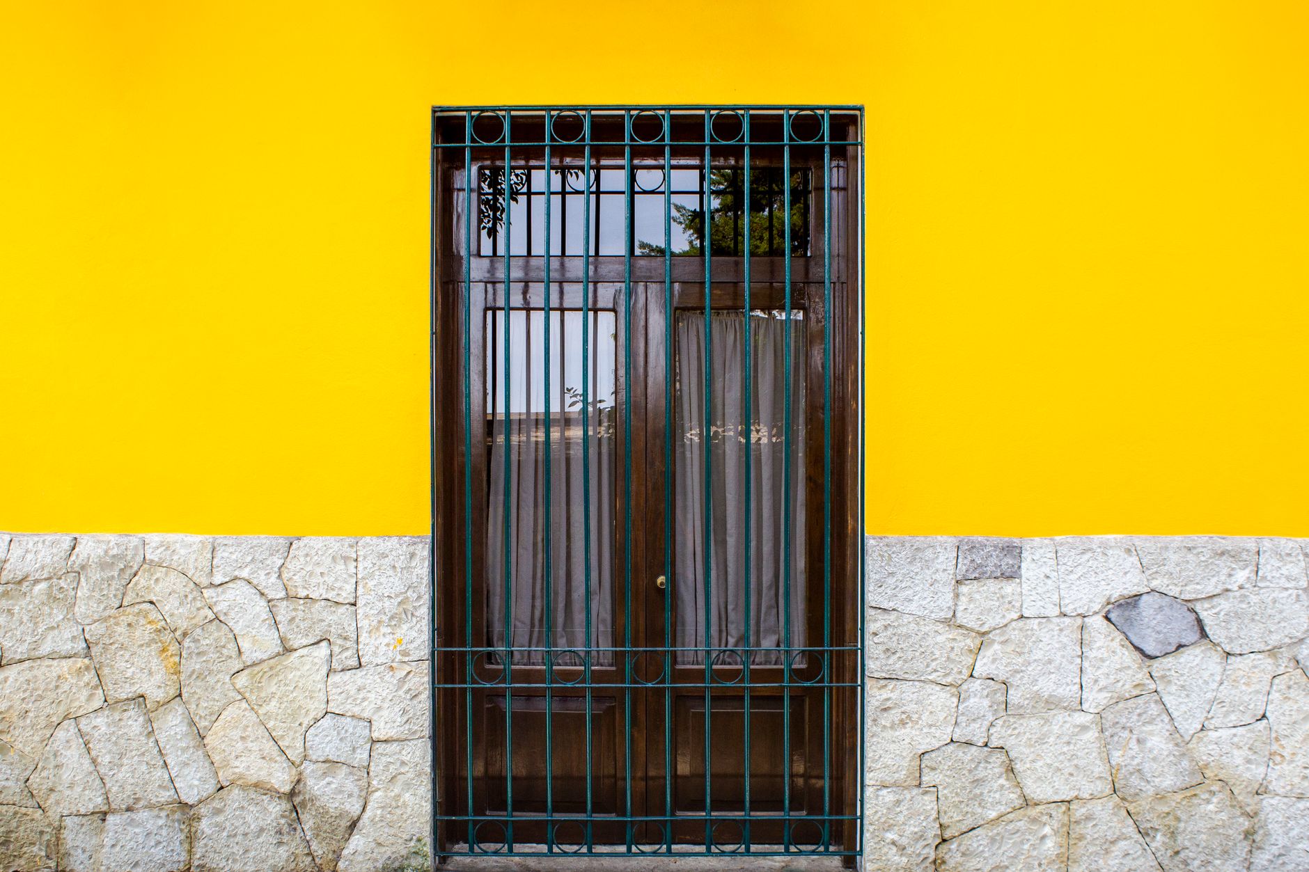 Exterior of wall with stony foundation and yellow wall with wooden door with metal gate in street in daytime outside