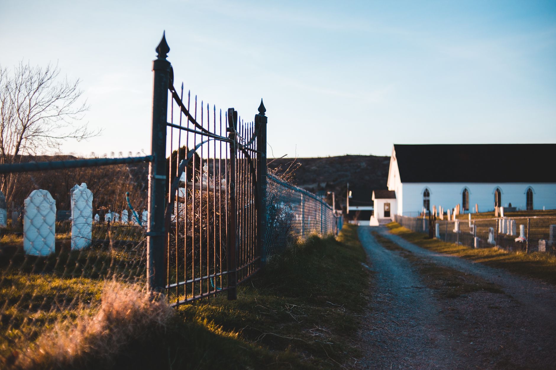 Ornamental metal fence near shabby pathway and old house in graveyard with headstones under sky